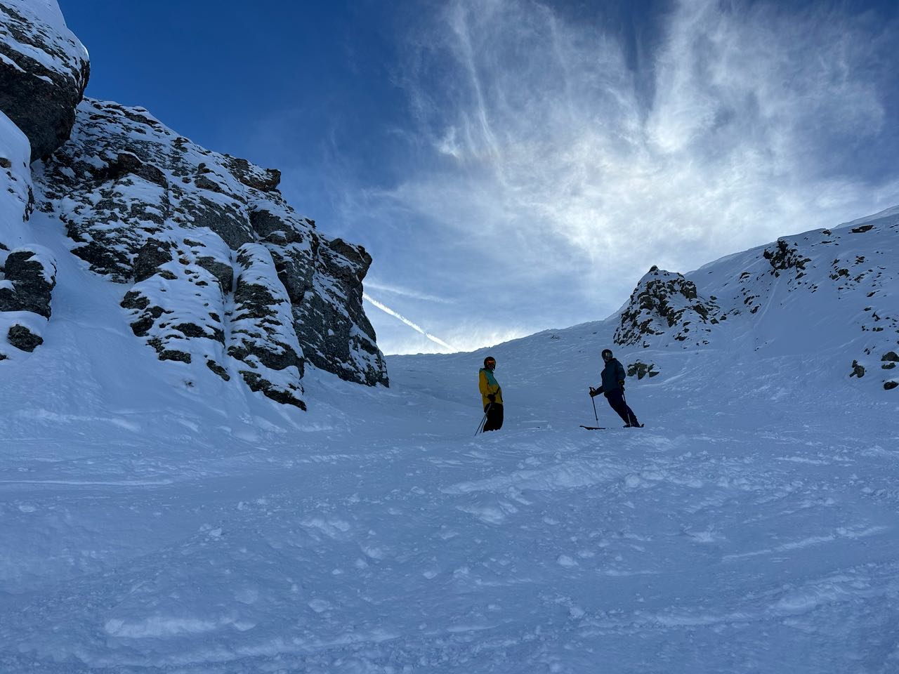 Two skiers at the bottom of a rocky snow chute